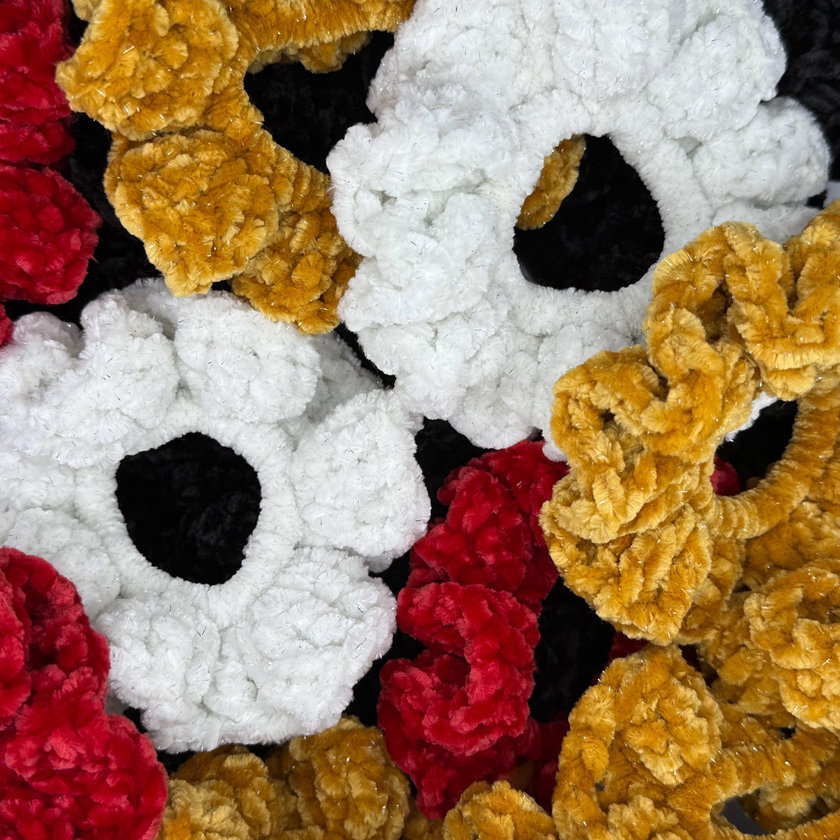 A collection of crocheted velvet scrunchies in white, red, black, and gold colors.